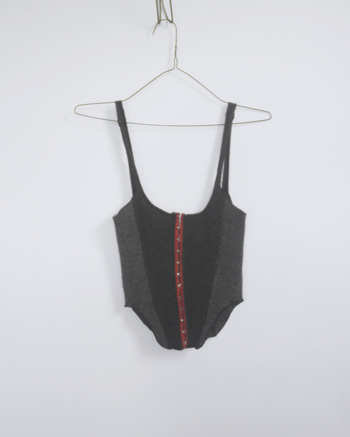 A dark gray cashemere hook and eye, corset style tank top with a red center panel, on a wire hanger against a plain white wall.