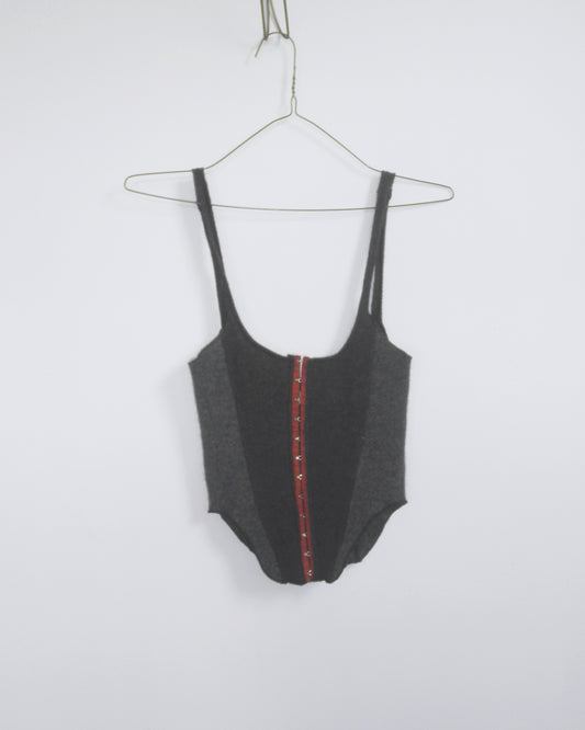 A dark gray cashemere hook and eye, corset style tank top with a red center panel, on a wire hanger against a plain white wall.